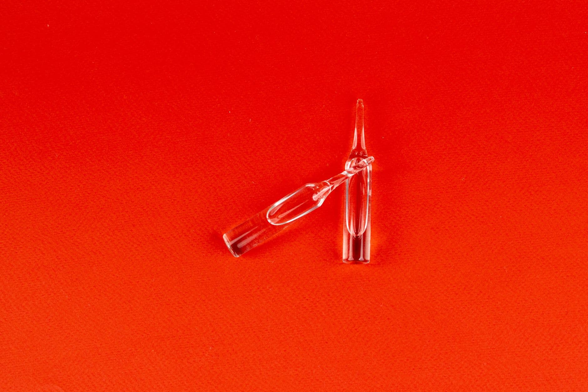 Two clear glass ampoules on a red surface.