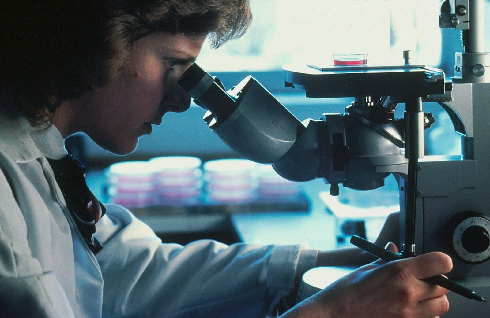 Laboratory technician examining a sample through a microscope.